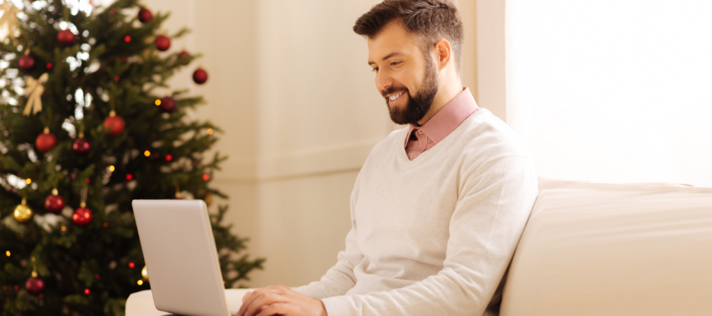 Man smiling while working on a laptop during the holiday season